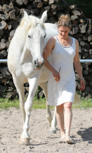 Frau mit weißem Kleid neben weißem Pferd