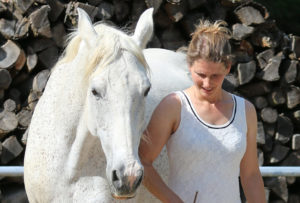 Weißes Pferd mit Frau im weißen Kleid am Boden in Verbindung miteinander.